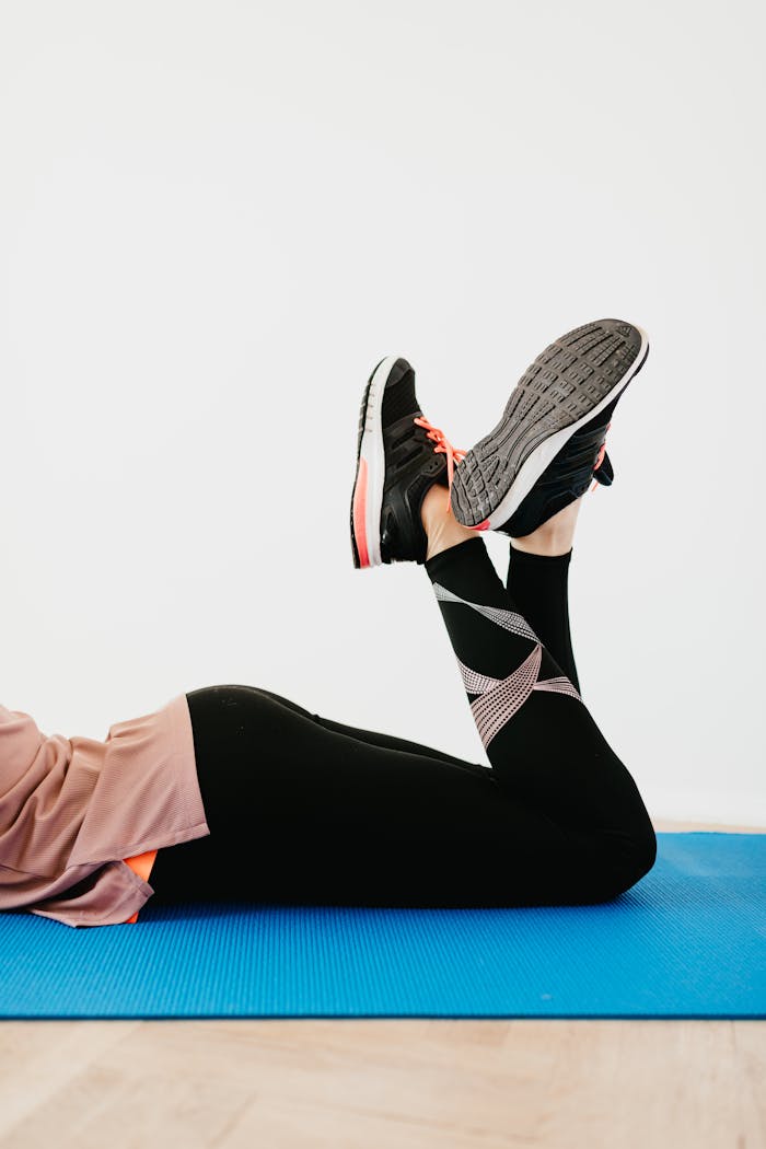 our-services-2 A woman in black leggings lying on a blue exercise mat indoors, performing a fitness routine.